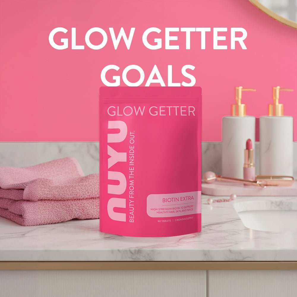 NUYU Biotin Extra pink supplement bottle on marble surface with towels and cosmetics for hair skin and nail support