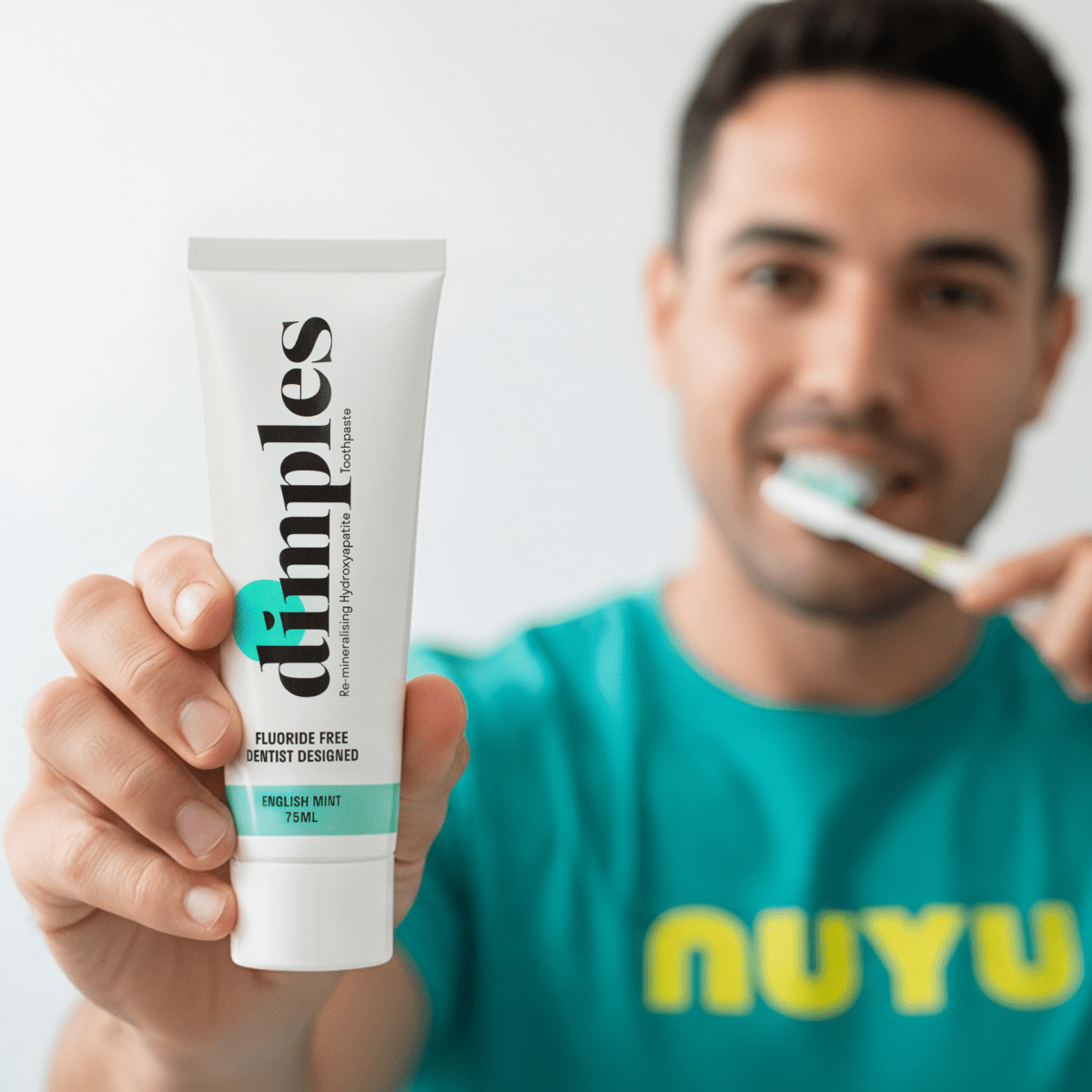 NUYU Dimples toothpaste tube held by man brushing teeth, wellness supplement UK brand