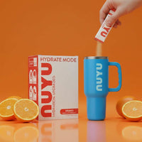 Hydrate Mode Orange sachet being poured into blue Nuyu cup with fresh oranges and product box on orange background for airborne vitamin c hydration boost