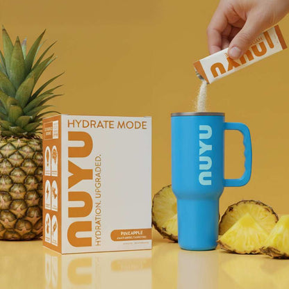 NUYU pineapple electrolyte sachets UK being poured into blue tumbler with fresh pineapple