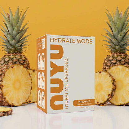 NUYU pineapple electrolyte sachets UK box with fresh cut pineapples on orange backdrop