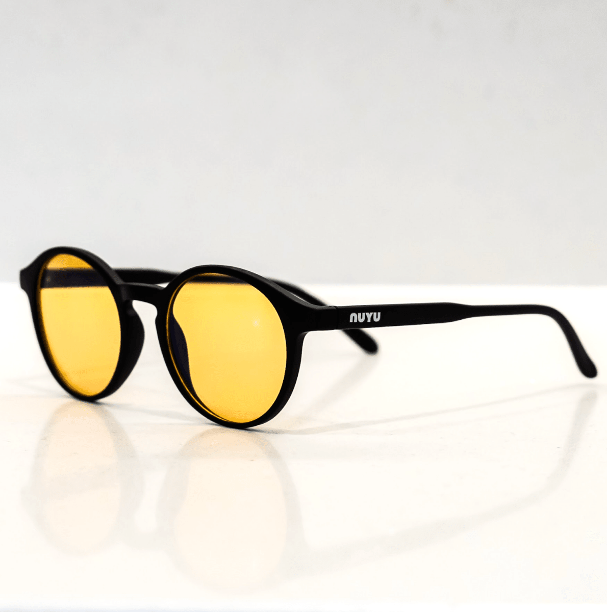 NUYU Afterlight blue light blocking glasses UK with yellow lenses on reflective white surface