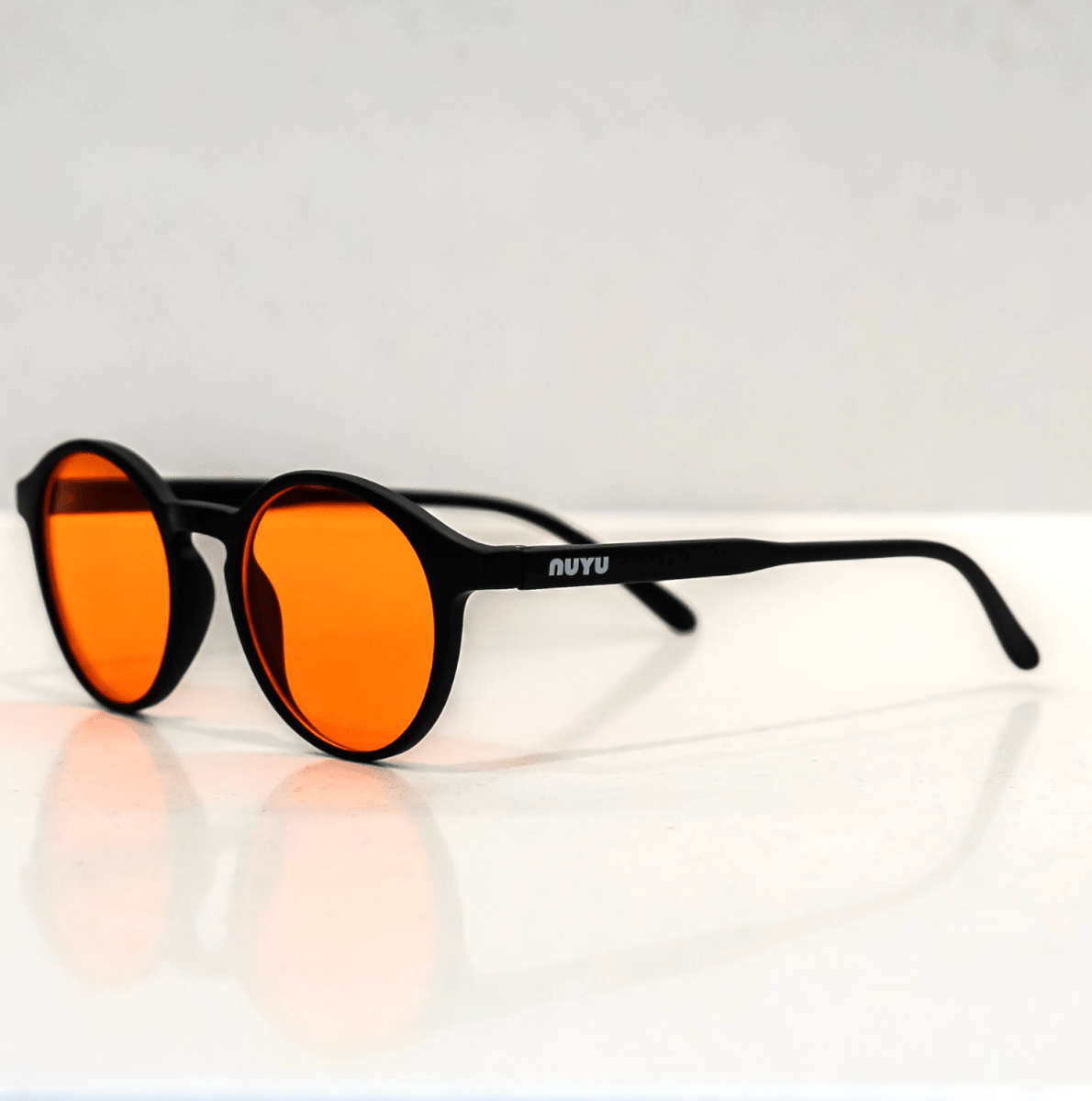 NUYU Afterlight blue light blocking glasses UK with orange lenses on reflective white surface