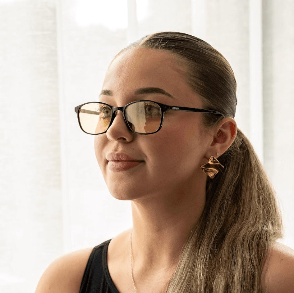 NUYU Afterlight blue light blocking glasses UK worn by woman with gold earrings by window