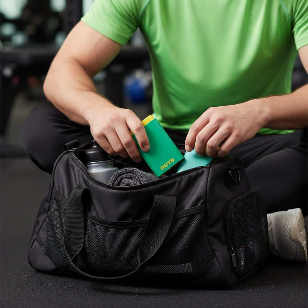 Person placing green and yellow NUYU Pocket Pack into gym bag with water bottle and towel in background