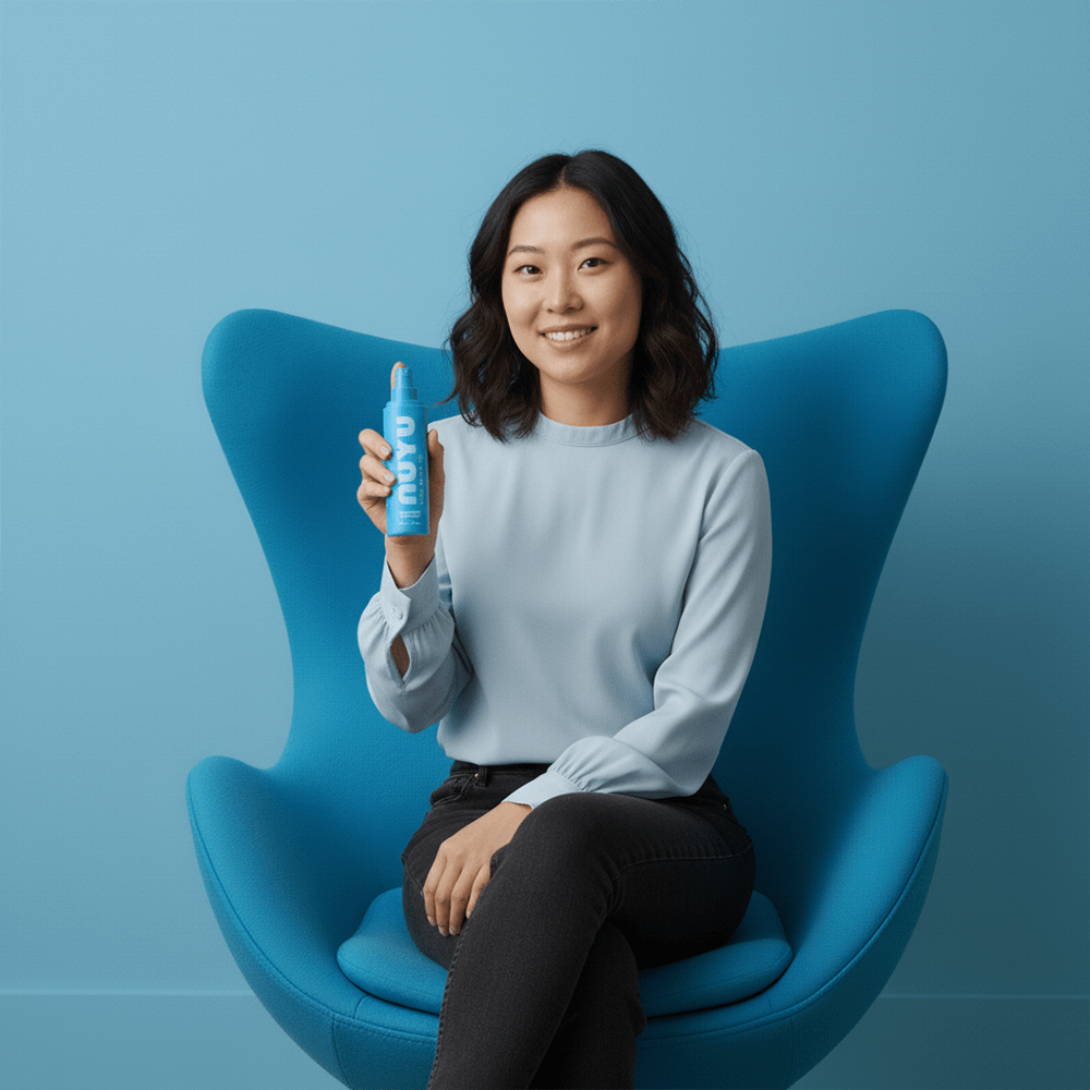 Woman sitting on a blue chair holding NUYU Sleep Magnesium Spray bottle with a smile against a blue background