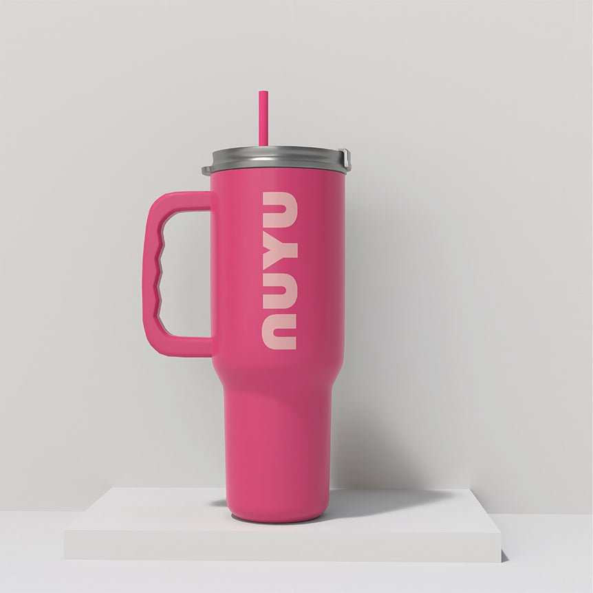 NUYU pink insulated tumbler with handle and straw on white platform against grey background