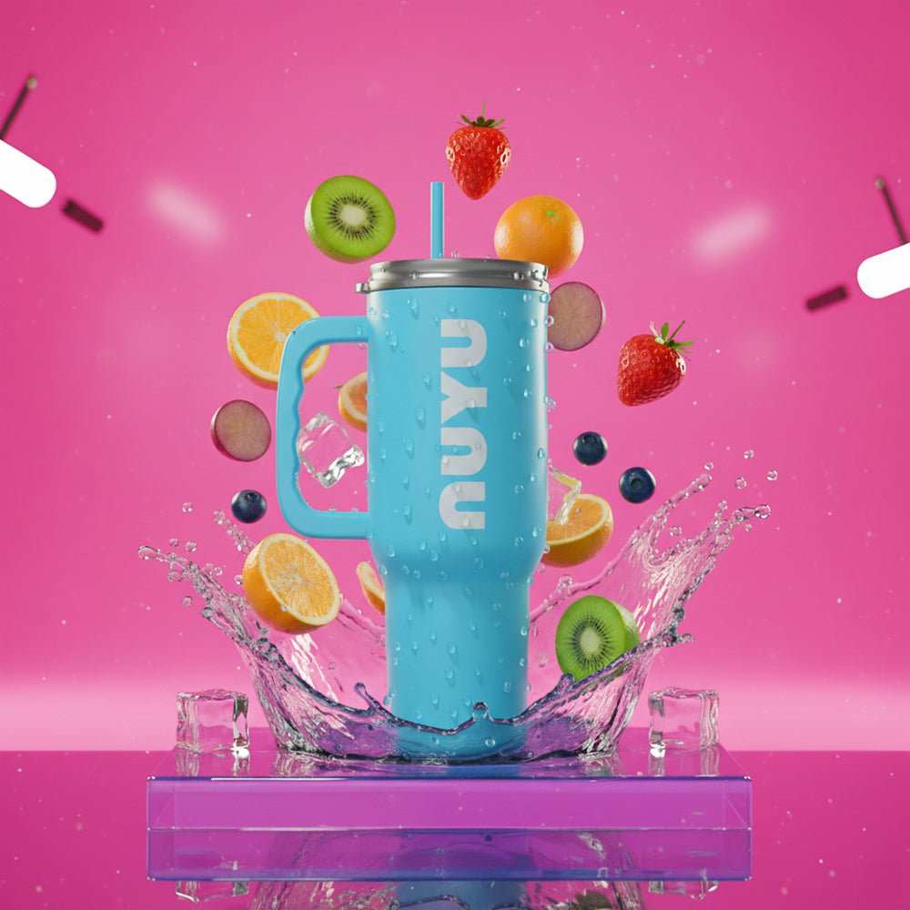 Blue stainless steel tumbler with handle surrounded by splashing water and floating fruits on pink background
