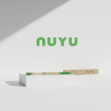 NUYU bamboo toothbrush with green bristles on white display stand, wellness supplement UK brand